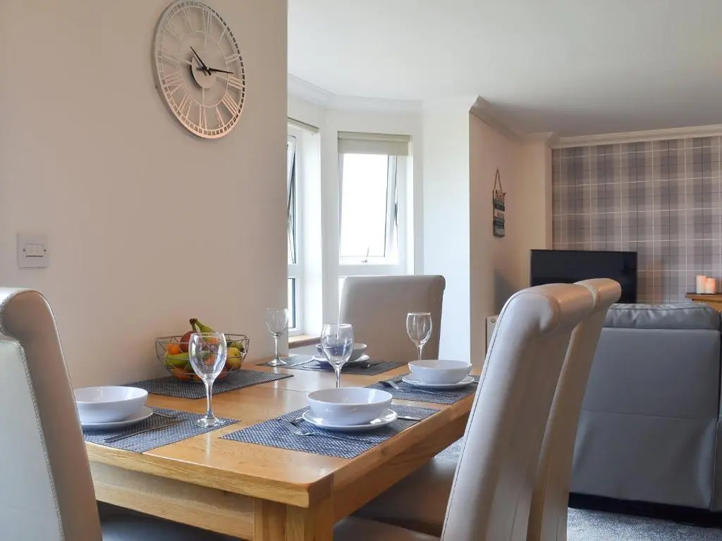 a dining room table with chairs and a clock on the wall at Aurora in Lossiemouth