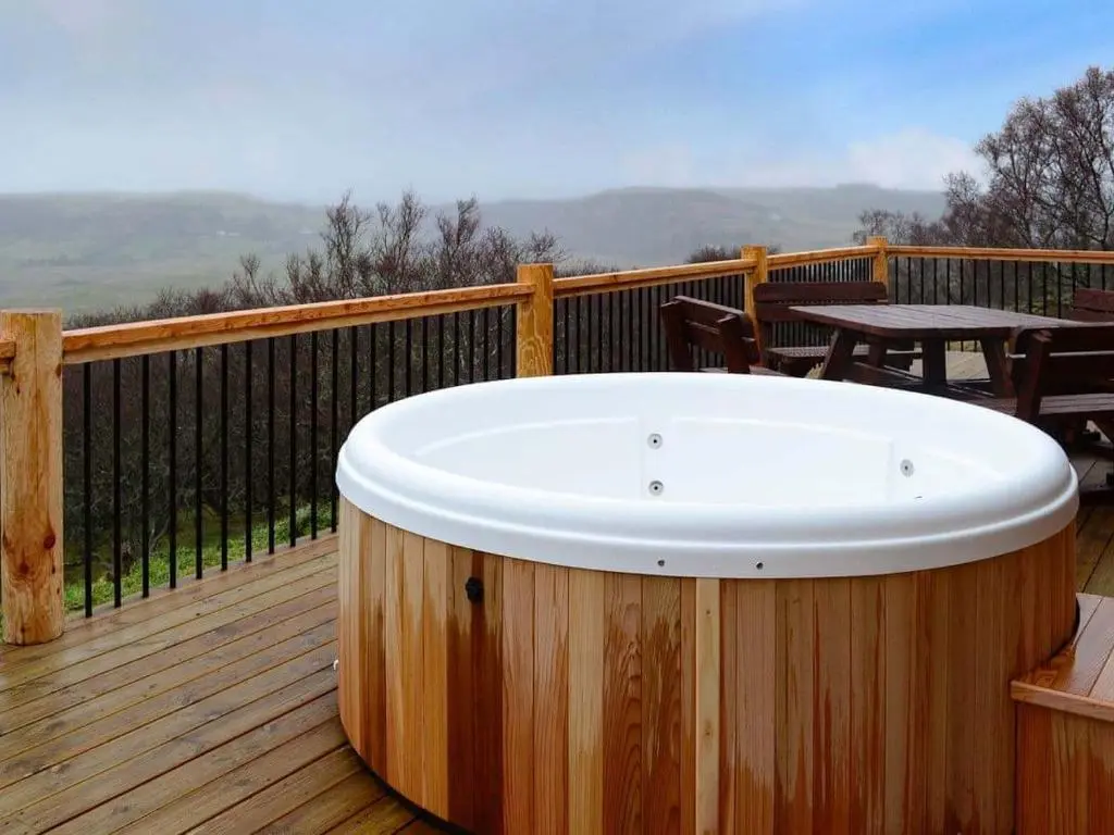 a hot tub on a wooden deck with a table at Red Kite & Osprey Lodges in Rhilochan