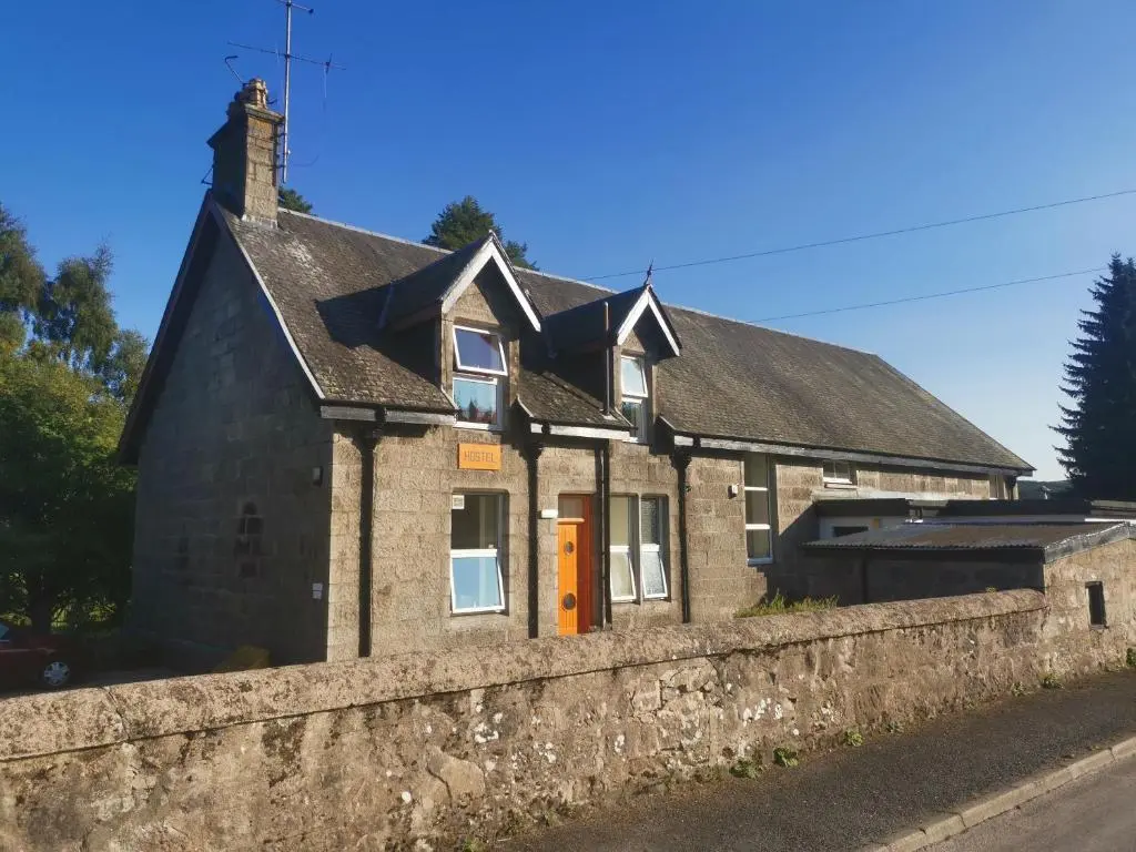an old stone house with a stone wall at Dalwhinnie Old School Hostel in Dalwhinnie