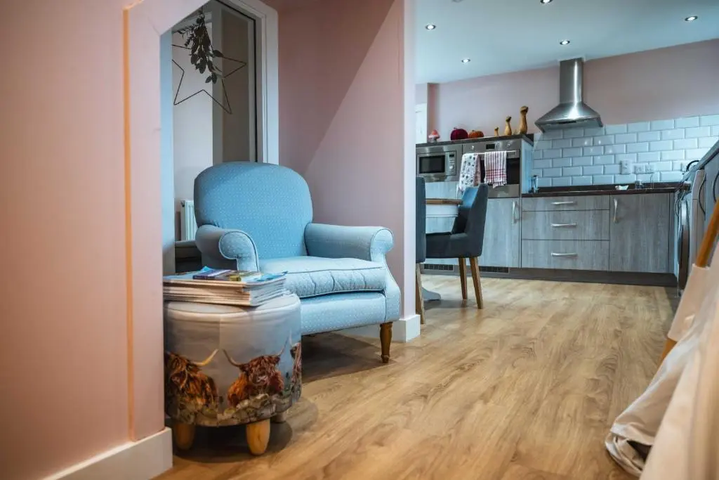 a living room with a blue chair and a kitchen at Bramble Cottage in Turriff