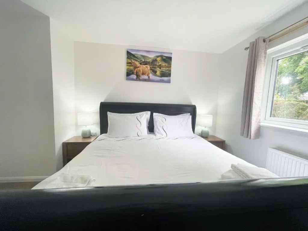a bedroom with a bed with white sheets and a window at Matara House Holiday Home in Inverness