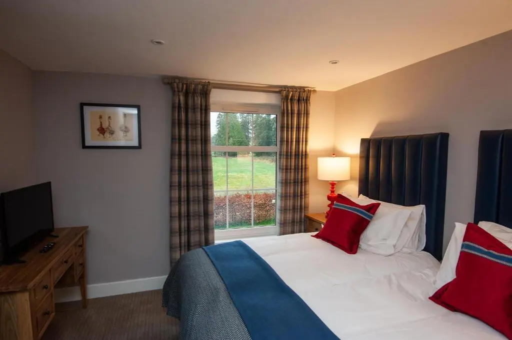 a bedroom with a bed with red pillows and a window at Parkside, The Loch Ness Cottage Collection in Inverness