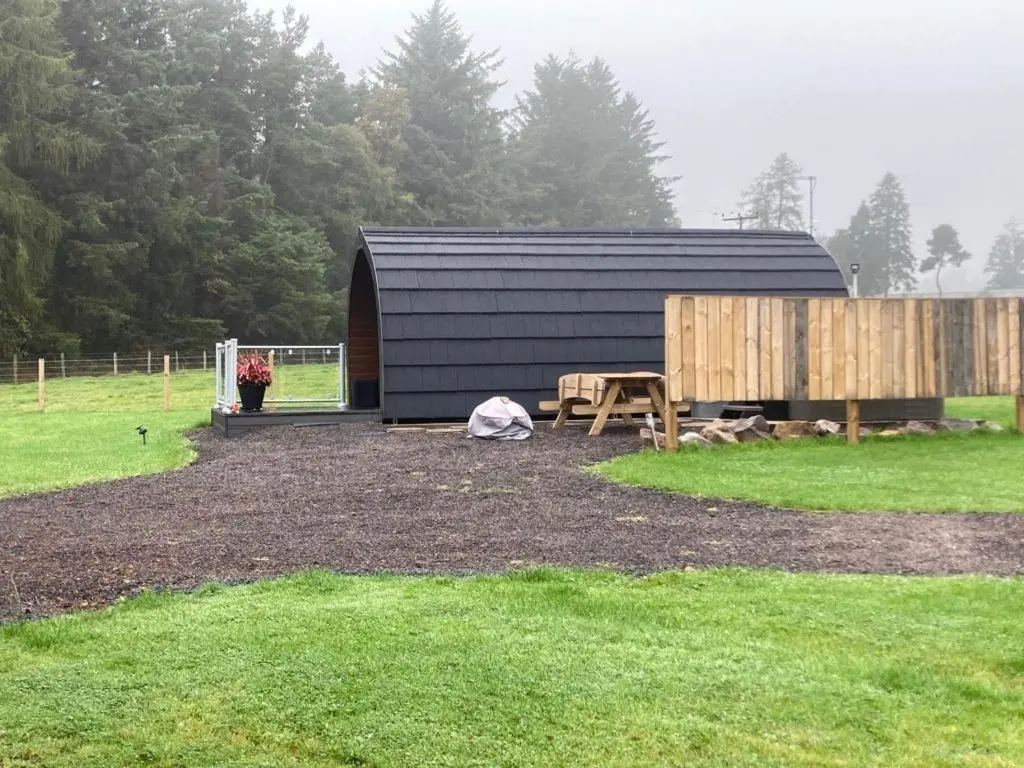 a black building with a picnic table and a wooden fence at Owls Retreat Glamping Pod with Hot tub in Keith