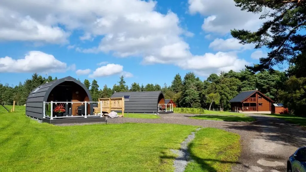 a barn and a house on a grass field at Owls Retreat Glamping Pod with Hot tub in Keith