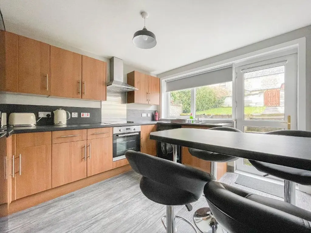 a kitchen with wooden cabinets and a table and chairs at Academy Street Cottage in Tain
