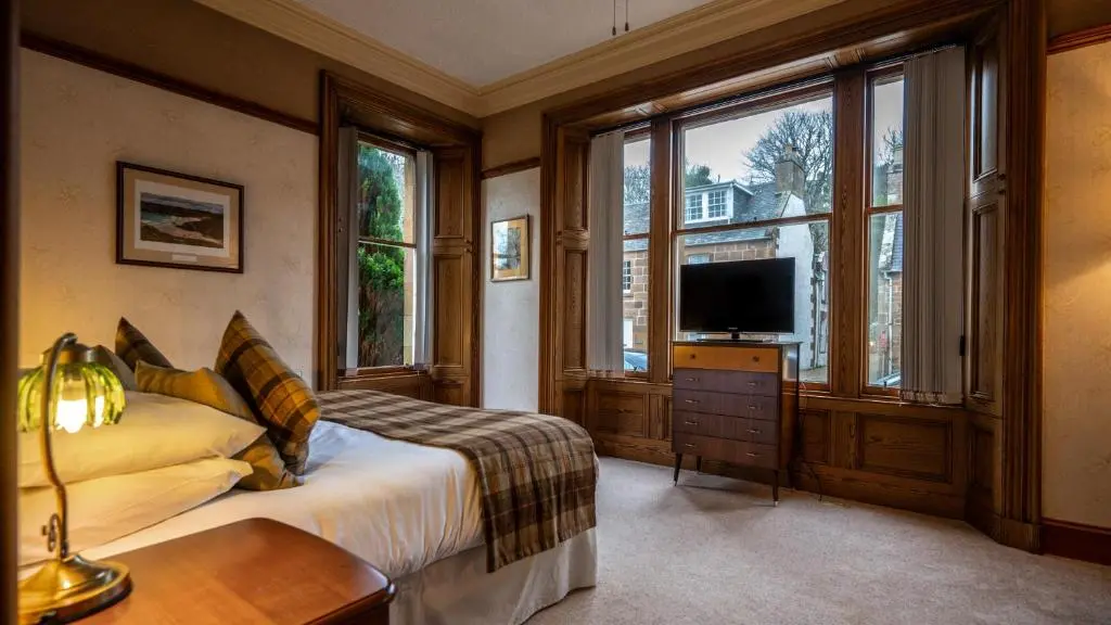 a bedroom with a bed and a tv and windows at The Old Bank House Self Catering Apartment Dornoch in Dornoch