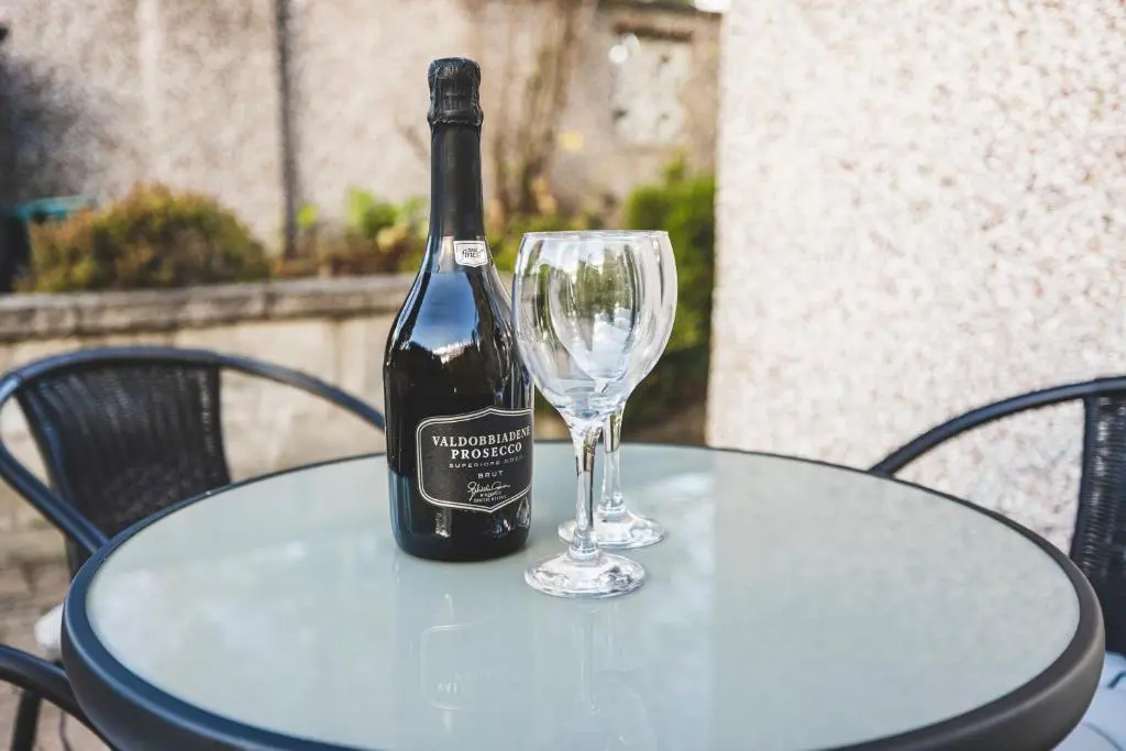 a bottle of wine sitting on a table with a glass at Bright House with Garden & Patio in Market Town in Inverurie
