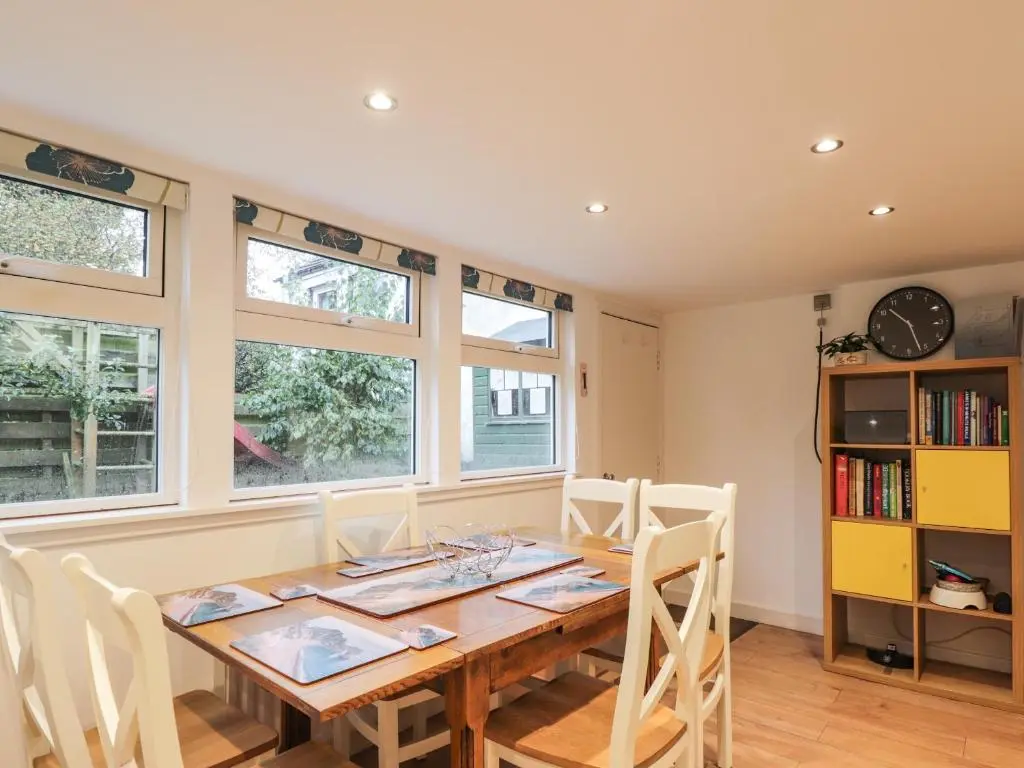 a dining room with a wooden table and some windows at 3 Dunrobin Street in Tain