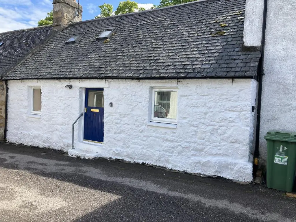a white cottage with a blue door and a trash can at 3 Dunrobin Street in Tain