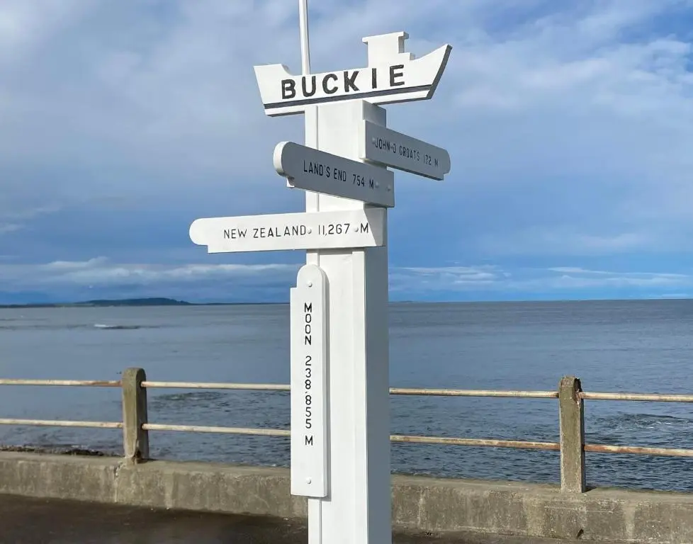 a white street sign with arrows in front of the ocean at Seaspray Cottage in Buckie