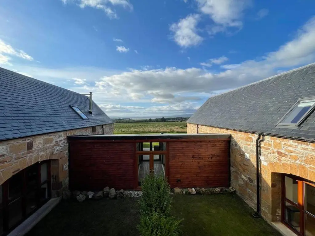 a brick building with a garage and a roof at Balloan Steading East in Dornoch