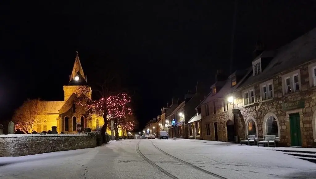 a snowy street at night with a church at Balloan Steading East in Dornoch