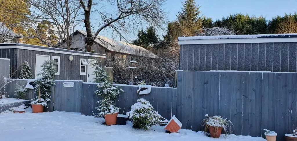a fence with potted plants in a yard covered in snow at Kingussie Garden Cabins in Kingussie