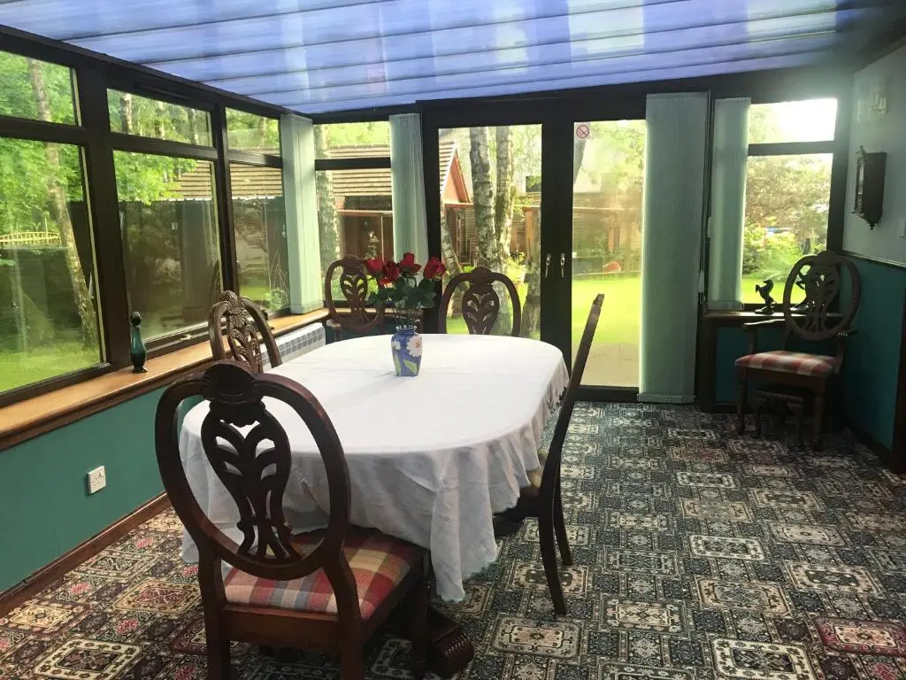 a dining room with a table and chairs and windows at Pine Chalet in Muir of Ord