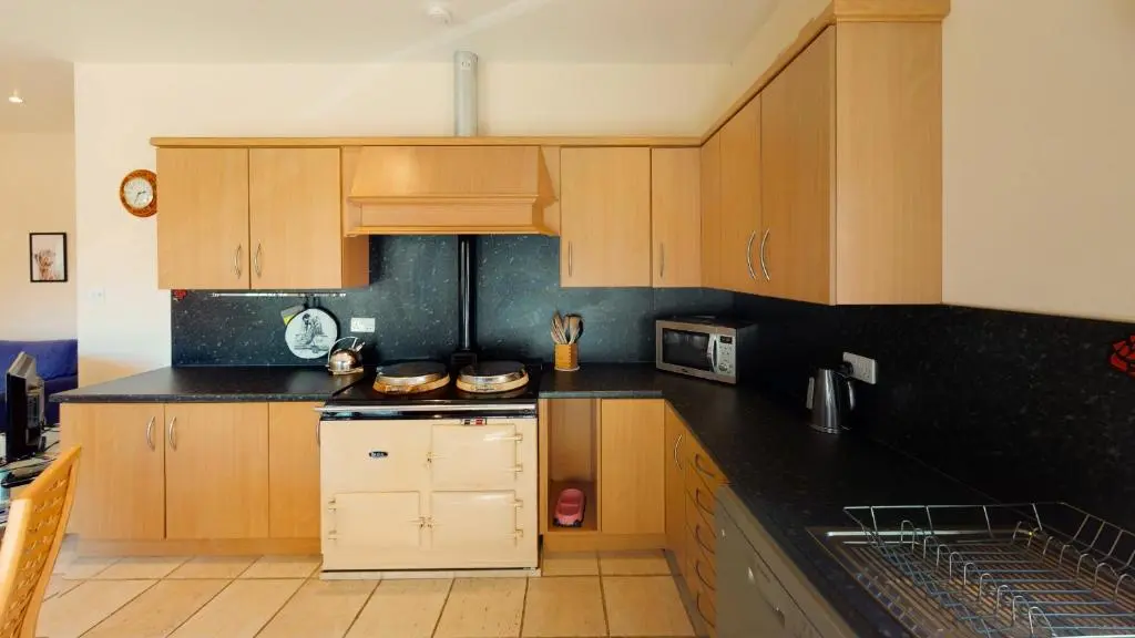 a kitchen with wooden cabinets and black counter tops at Druim An Lochain Cottage in Kinrara