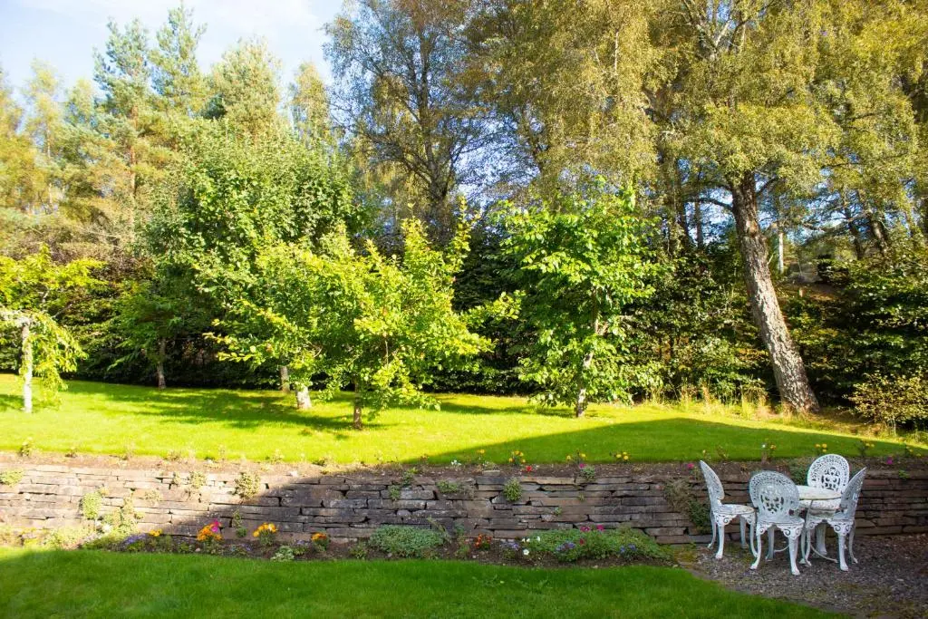two chairs and a table in a garden at Druim An Lochain Cottage in Kinrara