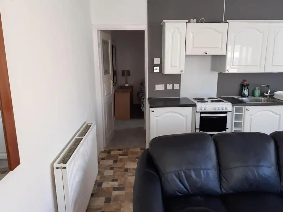 a kitchen with white cabinets and a couch in a room at Lossiemouth Seaside Flat in Lossiemouth