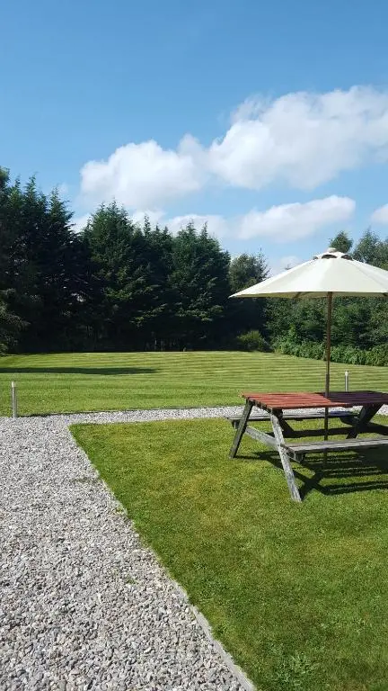 a picnic table with an umbrella on the grass at Torcroft Lodges in Drumnadrochit