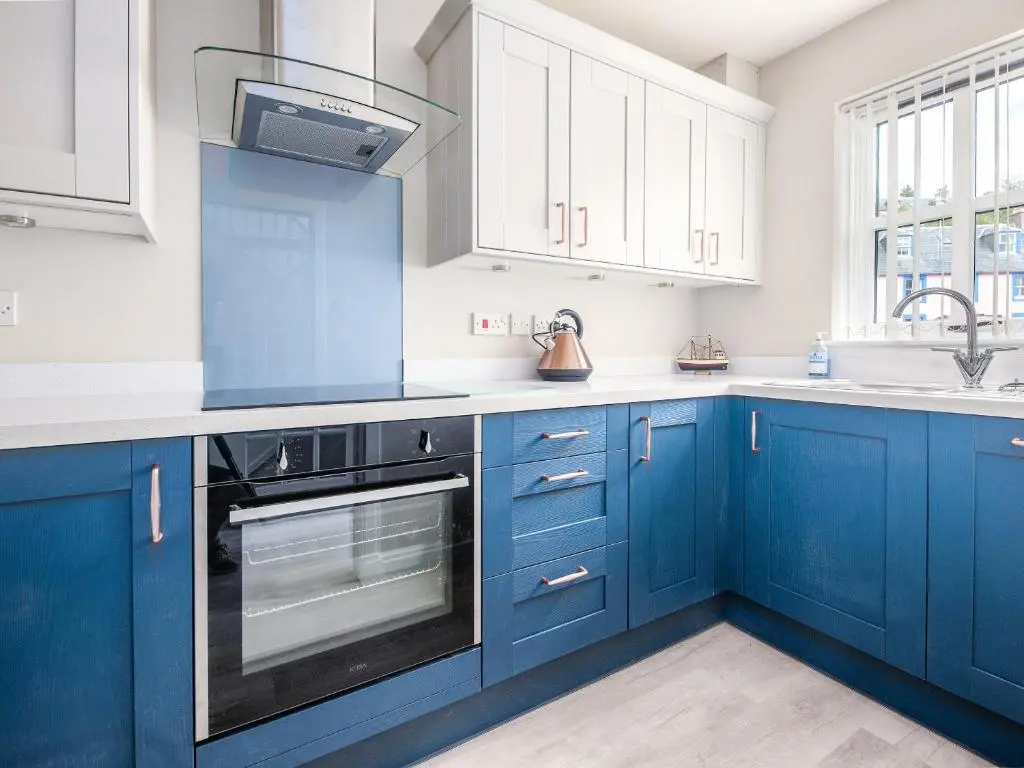 a blue kitchen with white cabinets and a sink at By The Sea in Avoch