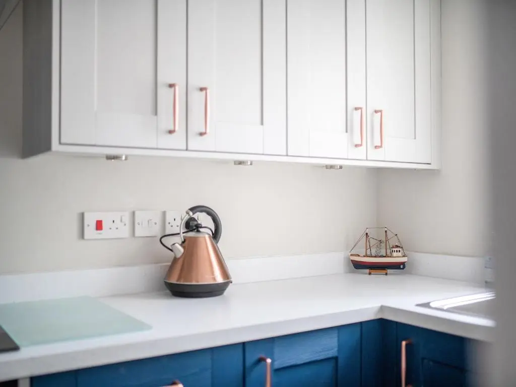 a kitchen with white cabinets and a tea kettle on the counter at By The Sea in Avoch