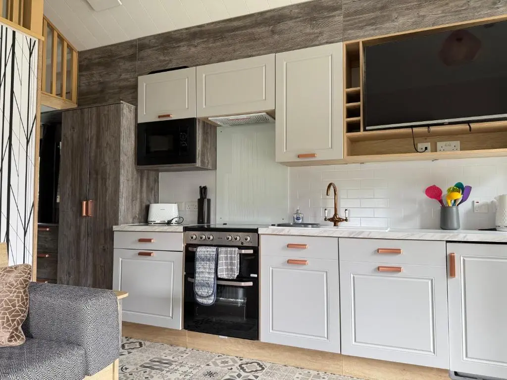 a kitchen with white cabinets and a black oven at The Parr Pod - Beautiful, luxury pod in Aberlour