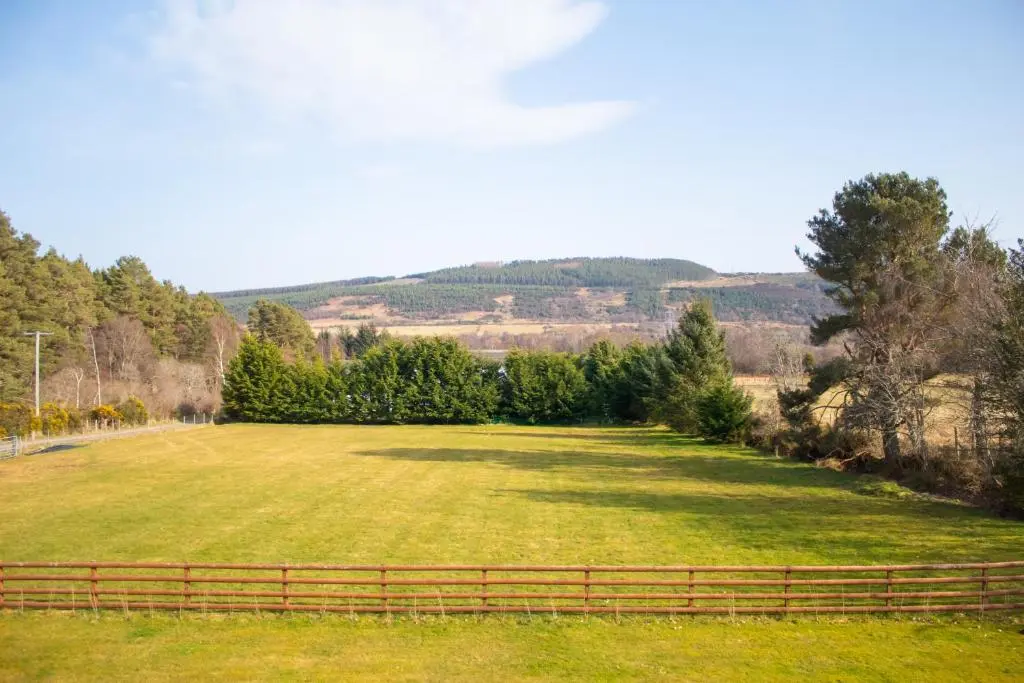 a large grassy field with a fence and trees at Longfield, Daviot in Inverness