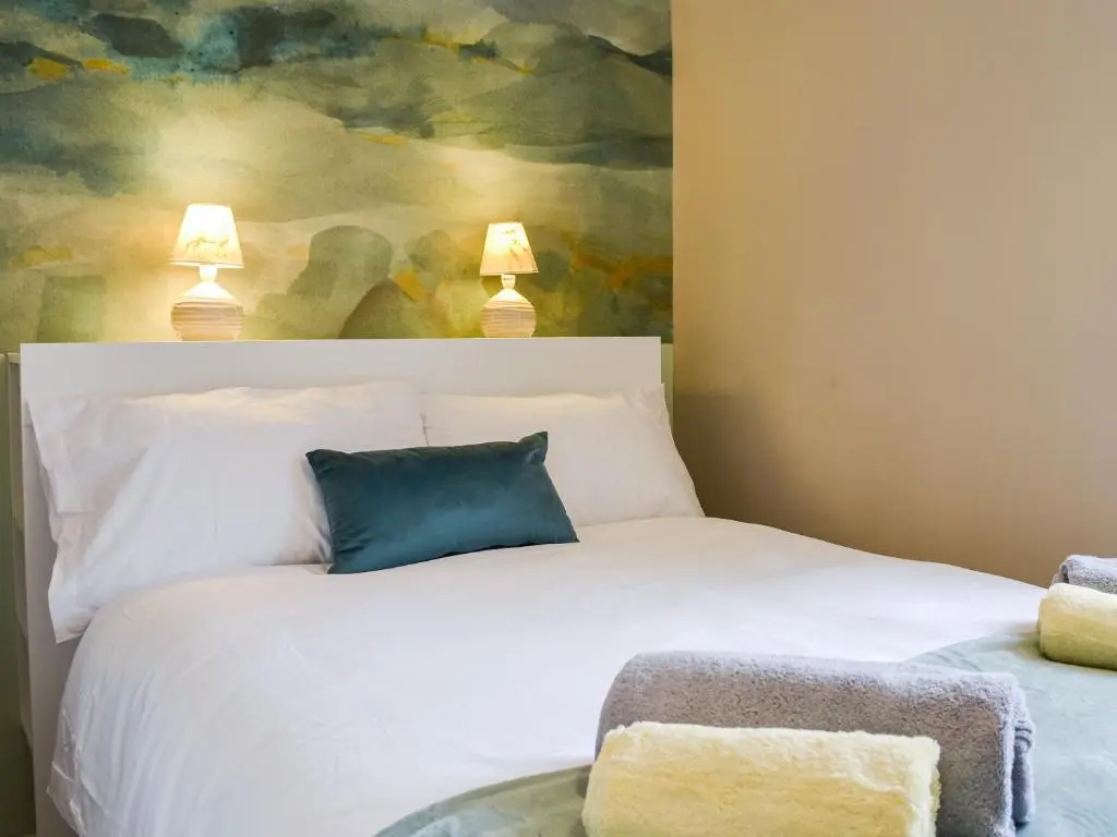 a bedroom with a white bed with a blue pillow at Riverside Cottage in Blair Atholl