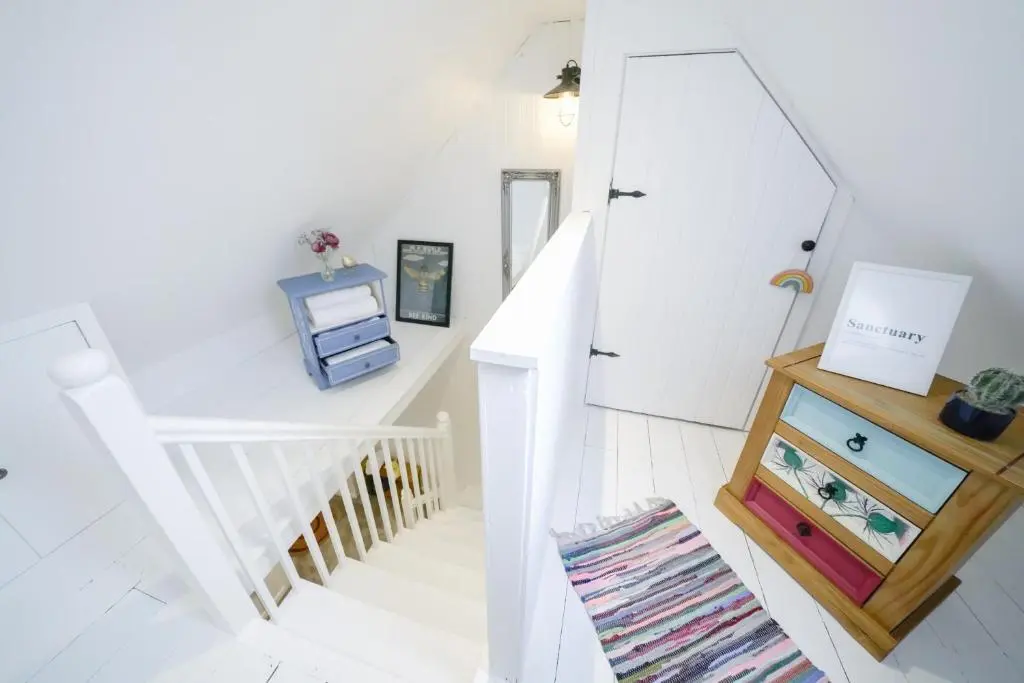 a white staircase with a mirror and a dresser at The Wee House by the Sea in Balintore
