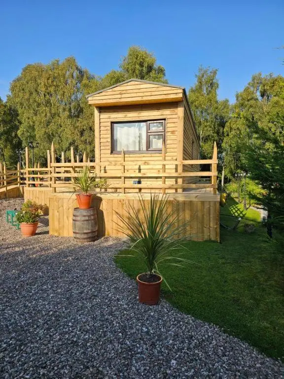 a wooden cabin with a fence and some plants at Highland Retreats Cannich in Cannich