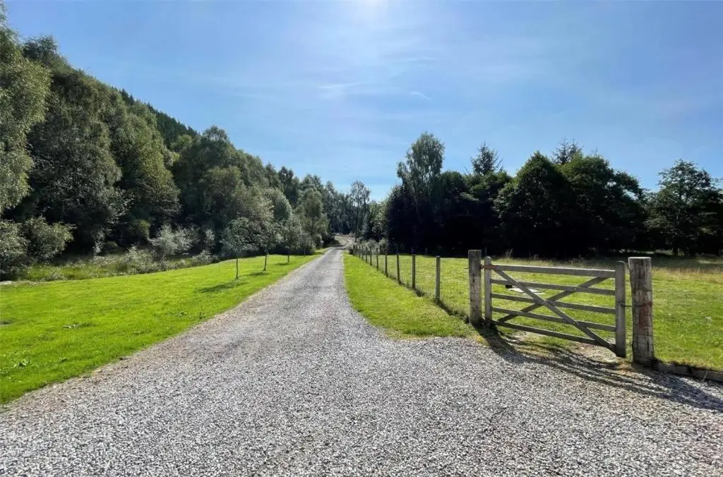 a gravel road with a fence next to a field at Highland Hideaway in secluded riverside location in Garve