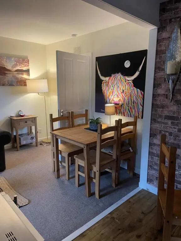 a dining room with a table and a bull painting on the wall at Charleston Apartment Self Catering 5 min drive from town centre in Inverness