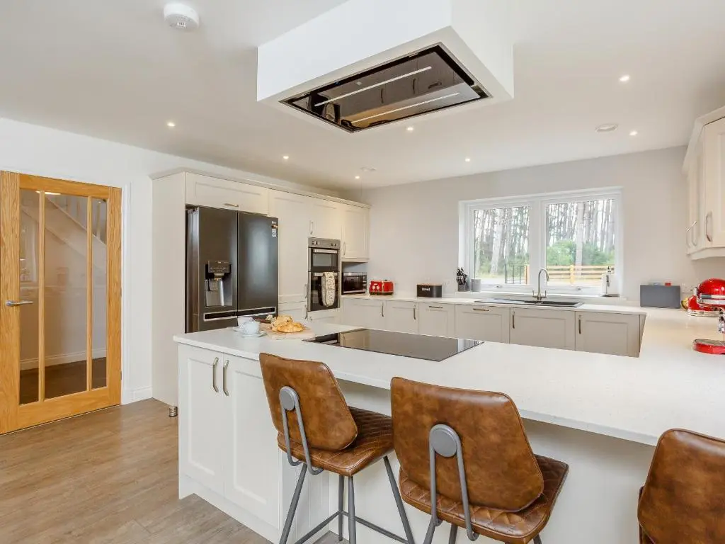 a kitchen with a large white counter and chairs at Strathclaggan in Aberlour