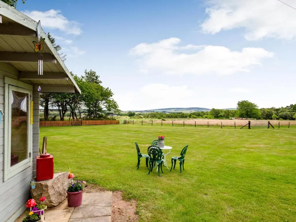 a patio with a table and chairs on a lawn at Glen Nevis Cottage in Port Elphinstone