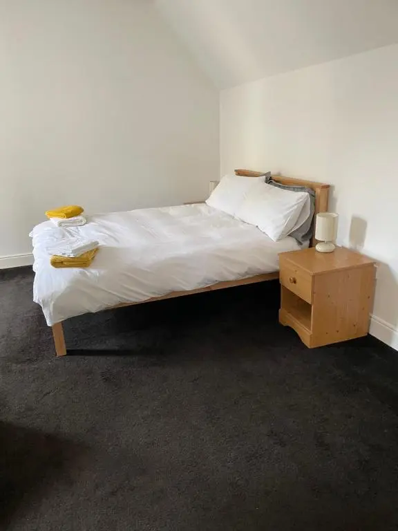 a bedroom with a bed with white sheets and a night stand at Newsagents Flat in Lairg