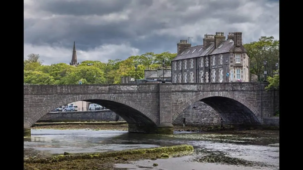 a stone bridge over a river with a building at Ella's Hoose in Wick
