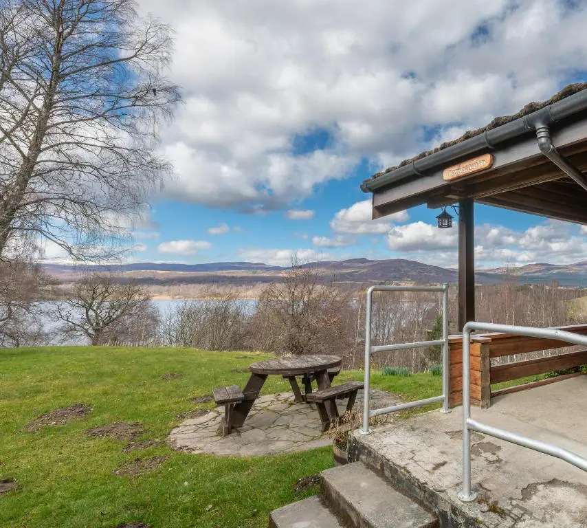 a picnic table in a field with a view of a lake at Loch Insh Chalets and Apartments in Kincraig