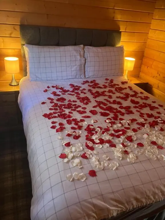 a bed with red roses on it with two lamps at Log Cabin in the City with hot tub in Culloden