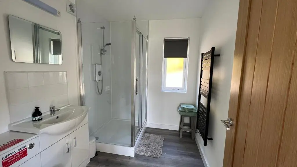 a white bathroom with a shower and a sink at Ceol Mor Highland Lodges in Lairg