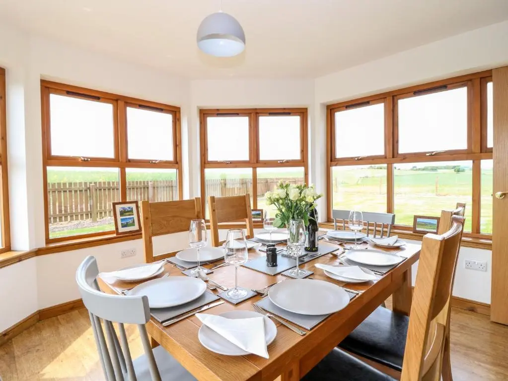 a dining room with a table and chairs and windows at Kilnary Cottage in Ellon