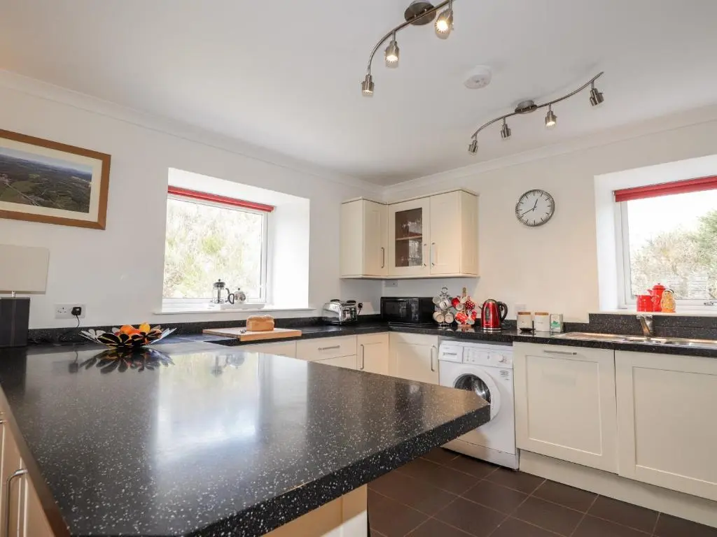 a kitchen with white cabinets and a black counter top at Redburn Steading in Nairn