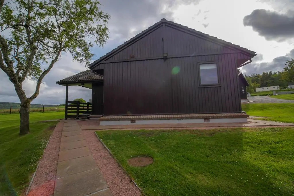 a black building with a tree in the grass at Glenview Chalet Park in Inverness