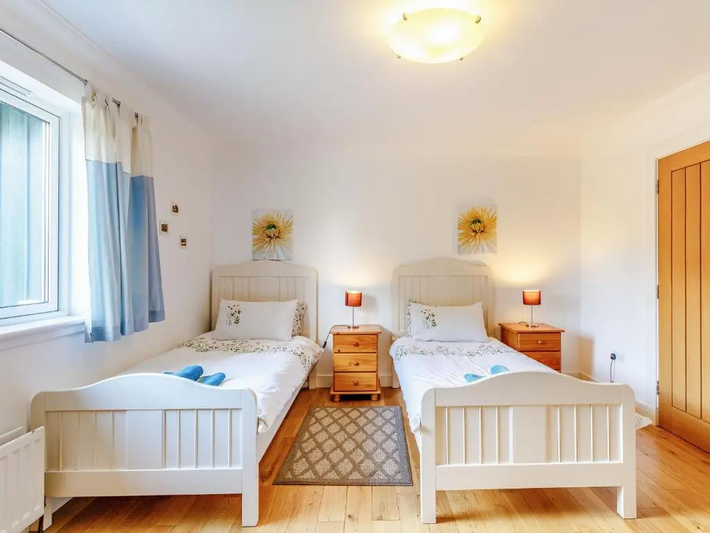 two beds in a room with white walls and wooden floors at Osprey Cottage- Ukc5519 in Boat of Garten