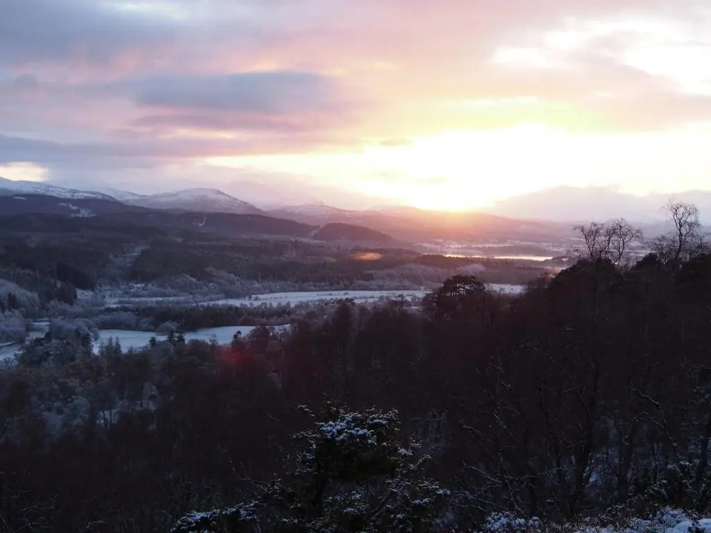 a sunset over a valley with a river and mountains at Ptarmigan in Nethy Bridge