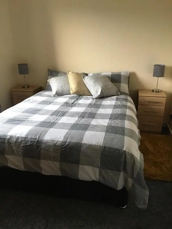 a bedroom with a bed with a plaid blanket and two night stands at No 5 Newly refurbished 4 bedroom house in Cononbridge