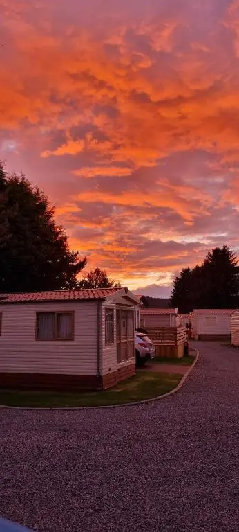 a small house in a parking lot with a sunset at The Wee Hoose in Boat of Garten