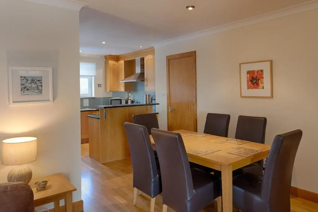 a dining room and kitchen with a wooden table and chairs at Links Apartment in Brora