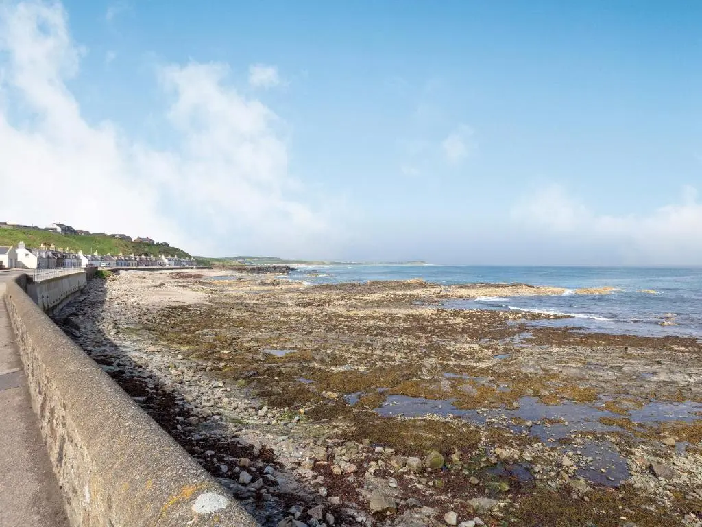 a beach with a retaining wall and the ocean at Headland View in Banff