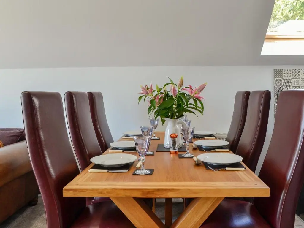 a wooden table with brown leather chairs and a table with plates and glasses at Queen's View Lodge in Inchmarlo
