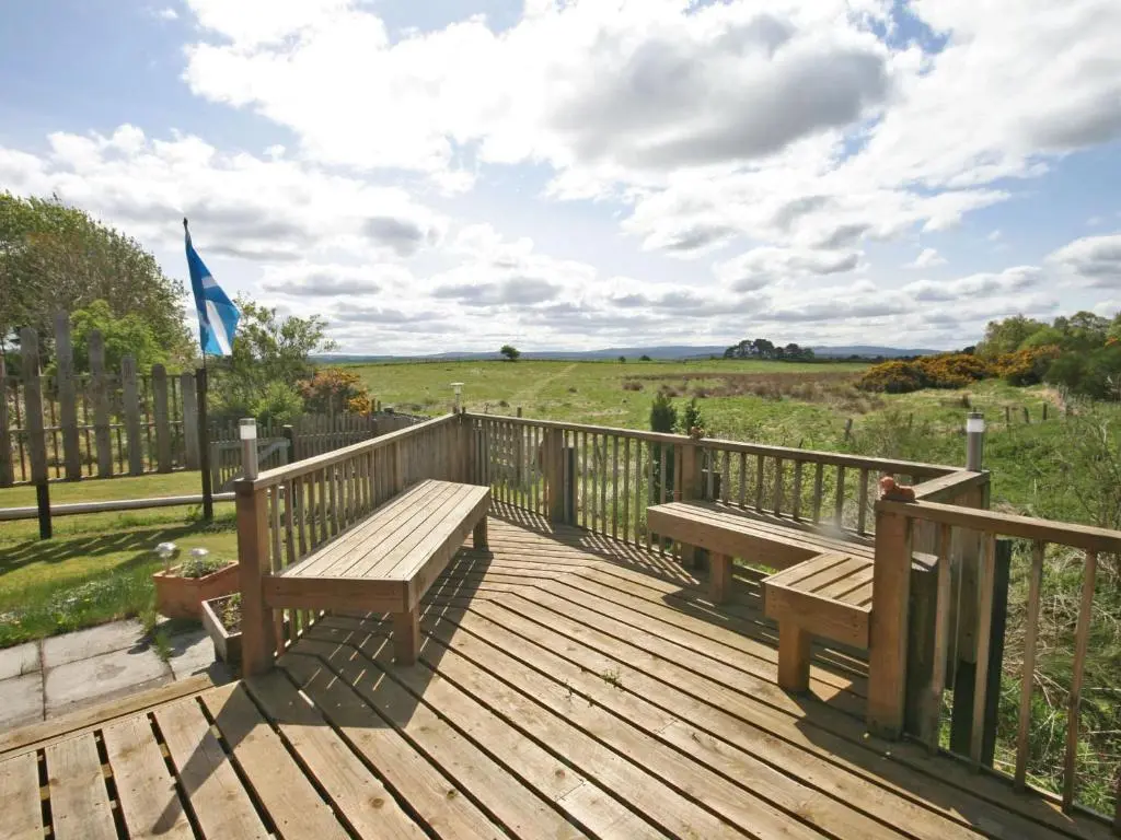 a wooden deck with two benches and a flag at Henrys Lodge in Balblair