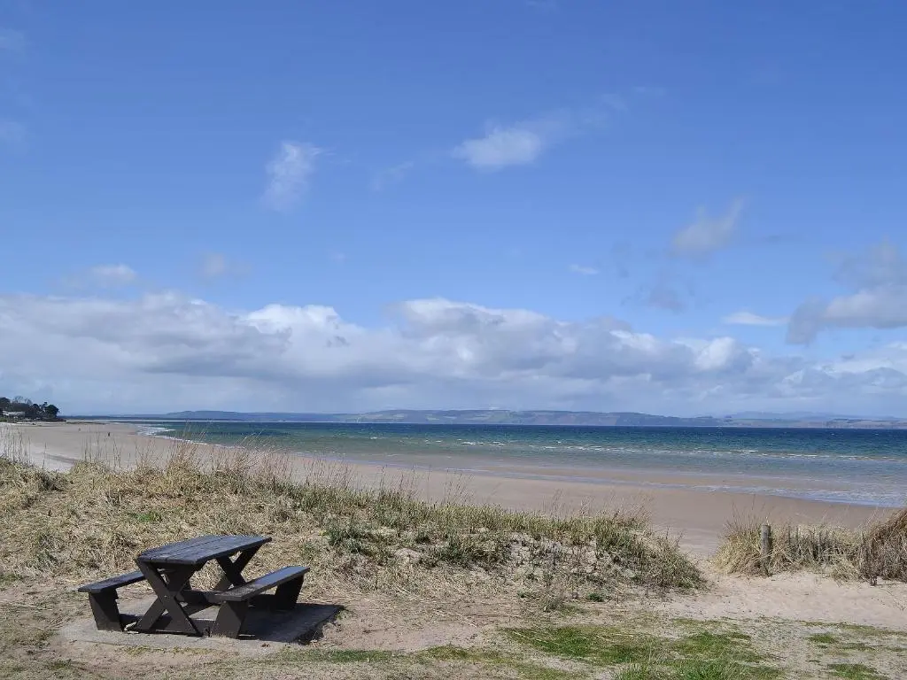 a bench sitting on the beach near the ocean at Henrys Lodge in Balblair
